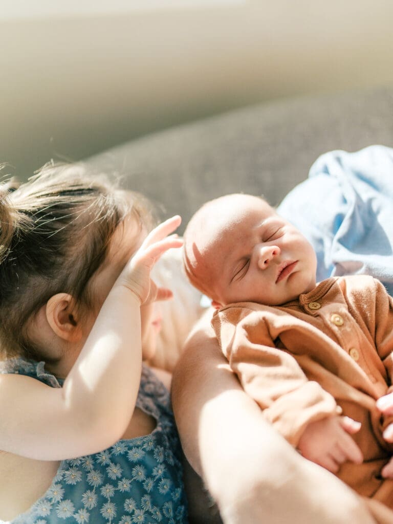 Little girl touching newborn baby brother's head in the soft sunlight filtering thru the windows in their living room