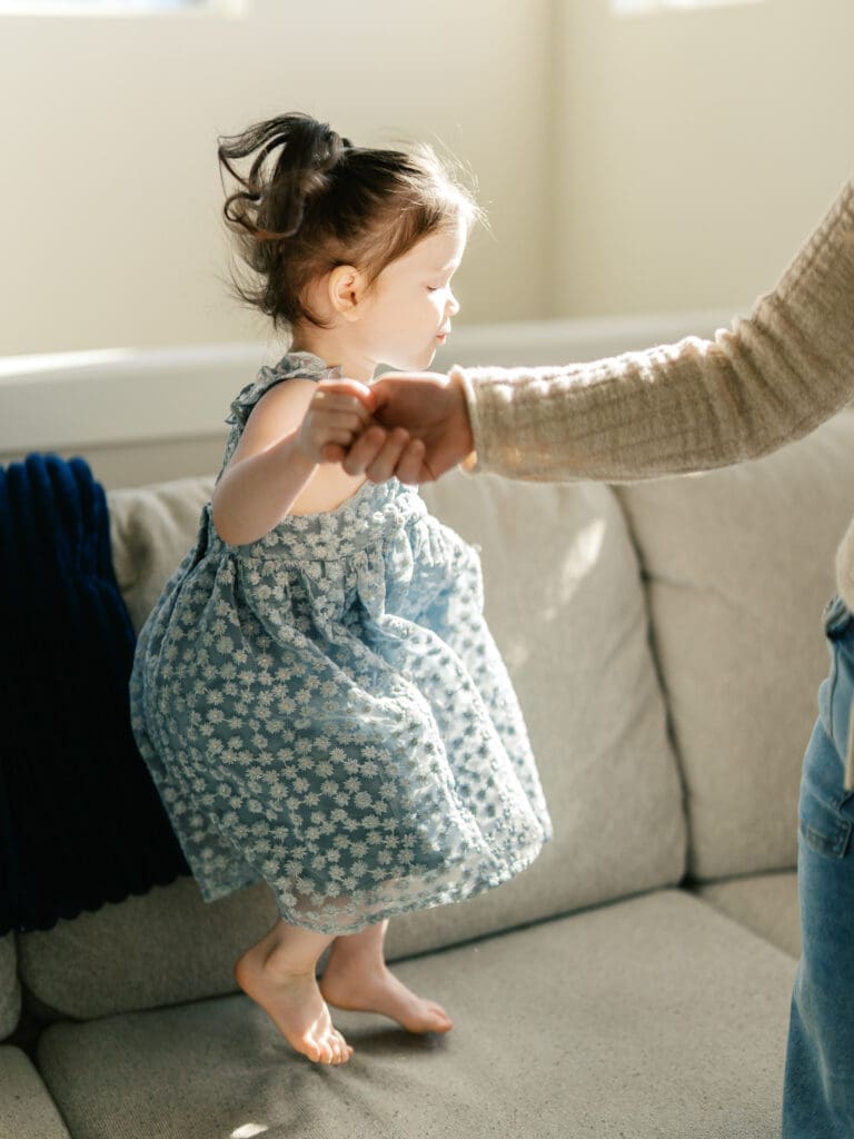 Little sister jumping on the couch while holding mom's hand